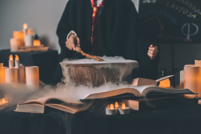 Person in Harry Potter robes waving a wand over a misty bowl